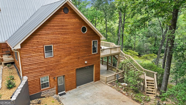 view of side of property with stairs, an attached garage, driveway, and metal roof