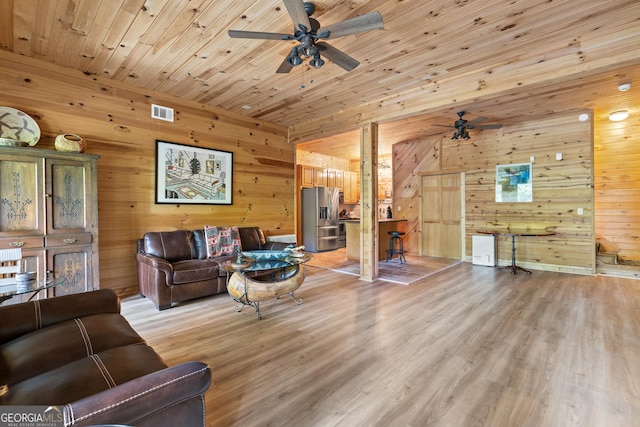 living area featuring light wood-type flooring, visible vents, wooden ceiling, wood walls, and ceiling fan