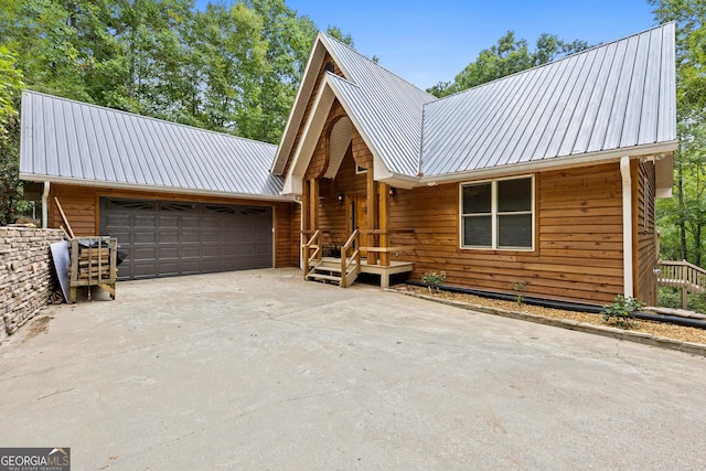 rustic home with an attached garage, metal roof, and driveway