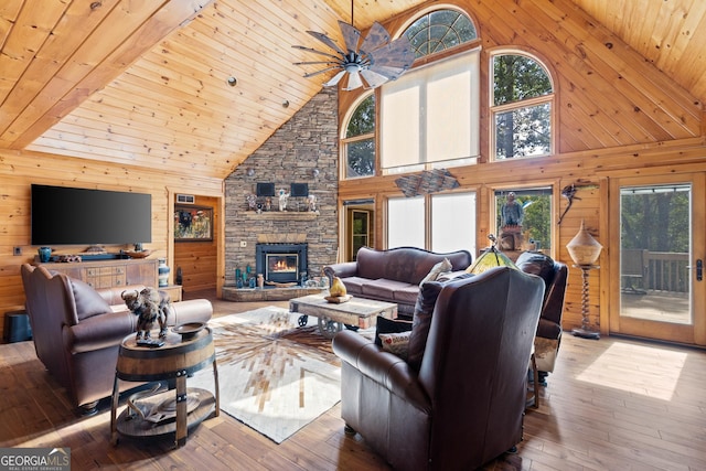 living room with hardwood / wood-style floors, ceiling fan, a stone fireplace, wood walls, and wooden ceiling