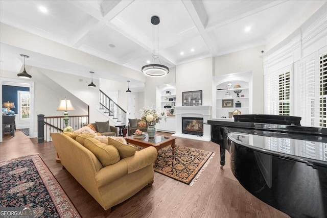 living area featuring built in shelves, wood finished floors, coffered ceiling, a glass covered fireplace, and beamed ceiling