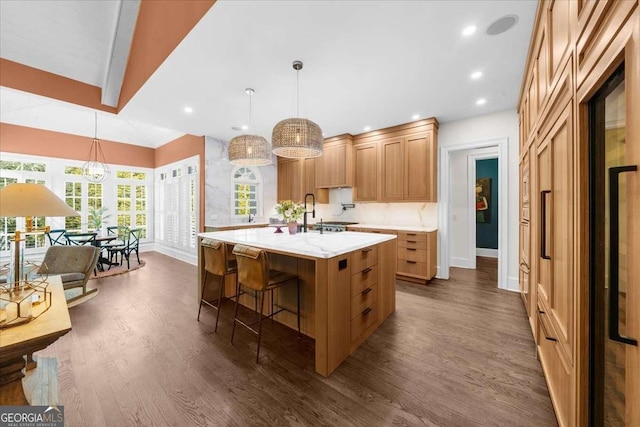 kitchen featuring dark wood finished floors, hanging light fixtures, an island with sink, and a kitchen bar