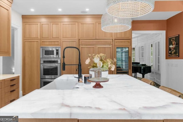 kitchen with a center island with sink, a sink, a kitchen breakfast bar, built in appliances, and light stone countertops