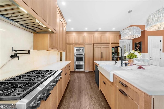 kitchen with light brown cabinetry, built in appliances, wall chimney exhaust hood, and a sink