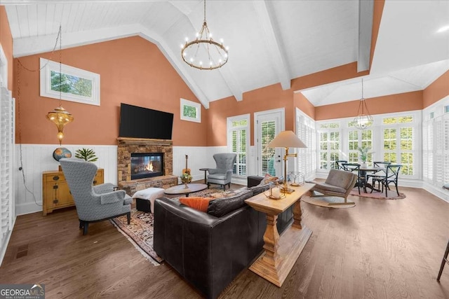 living room with a chandelier, a wainscoted wall, a stone fireplace, and wood finished floors