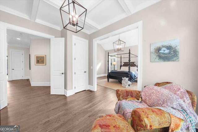 sitting room with a chandelier, coffered ceiling, baseboards, and wood finished floors