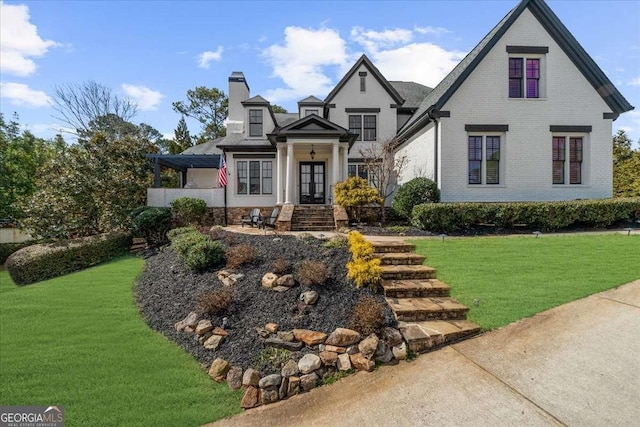 view of front of house with french doors, brick siding, a chimney, and a front yard