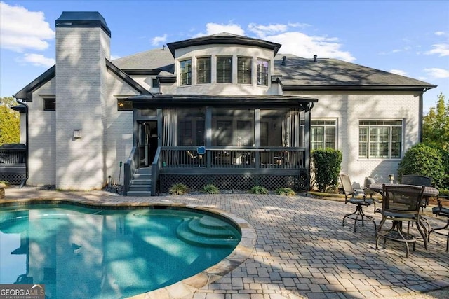 rear view of property with brick siding, a chimney, a patio, and a sunroom