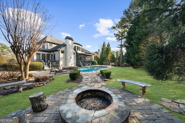 back of property featuring an outdoor pool, a fire pit, a lawn, and a patio area