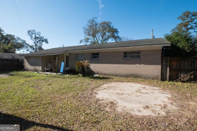 rear view of property featuring fence, brick siding, and a lawn