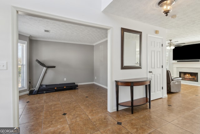 workout room with tile patterned flooring, a lit fireplace, ornamental molding, a textured ceiling, and a ceiling fan