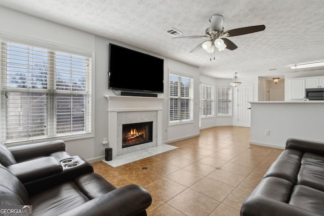 living area featuring visible vents, a textured ceiling, light tile patterned floors, a premium fireplace, and ceiling fan