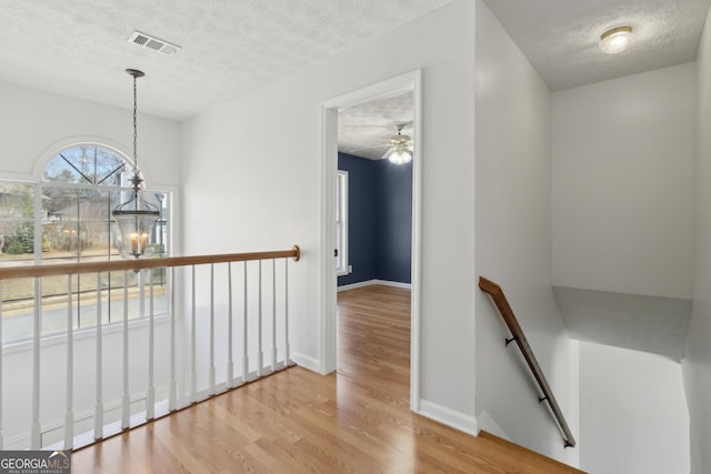 corridor with wood finished floors, visible vents, a textured ceiling, an upstairs landing, and a chandelier