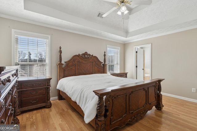 bedroom with a raised ceiling, light wood-style flooring, and visible vents