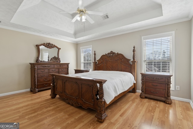 bedroom featuring a raised ceiling, a textured ceiling, and light wood finished floors