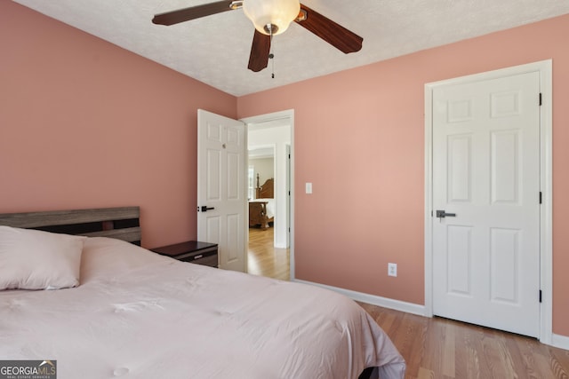 bedroom featuring light wood-style flooring, a textured ceiling, baseboards, and ceiling fan