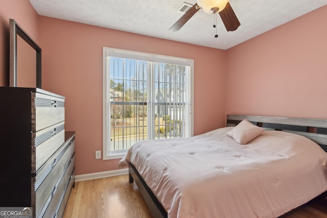 bedroom featuring visible vents, a textured ceiling, wood finished floors, baseboards, and ceiling fan