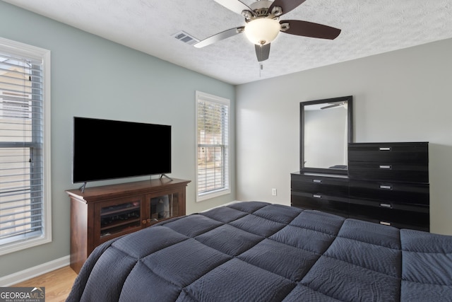 bedroom with visible vents, baseboards, wood finished floors, a textured ceiling, and a ceiling fan