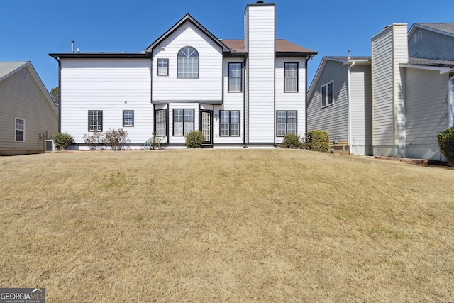 rear view of property with cooling unit, a chimney, and a yard