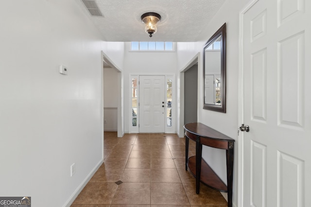 foyer entrance with tile patterned floors, visible vents, a textured ceiling, and baseboards