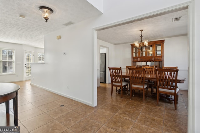 tiled dining space featuring baseboards, visible vents, a chandelier, and a textured ceiling