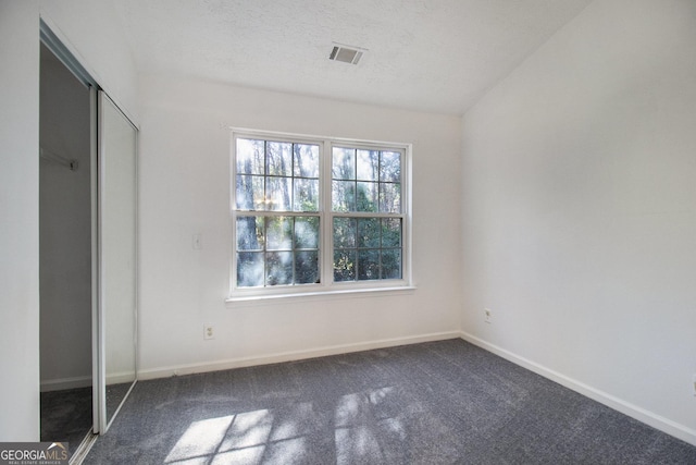 unfurnished bedroom with visible vents, a textured ceiling, baseboards, and dark colored carpet