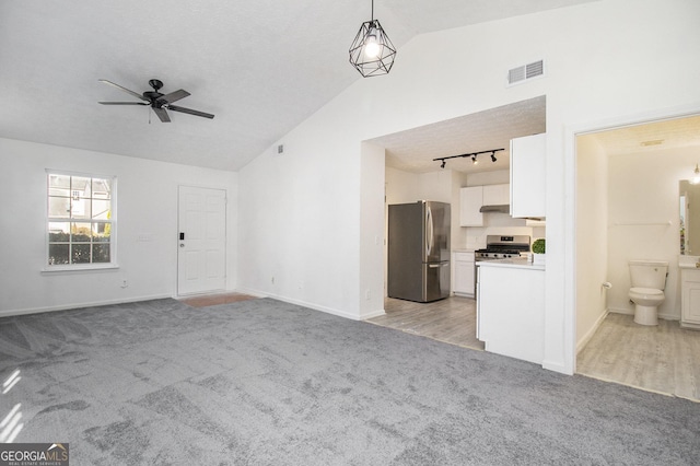 unfurnished living room featuring visible vents, track lighting, light colored carpet, lofted ceiling, and a ceiling fan