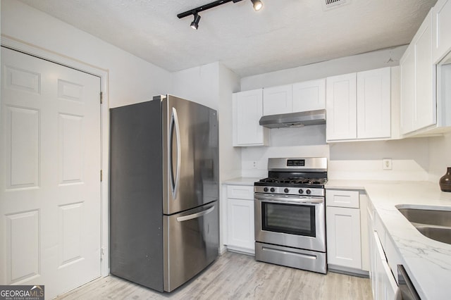 kitchen with a textured ceiling, white cabinets, under cabinet range hood, appliances with stainless steel finishes, and light wood-type flooring