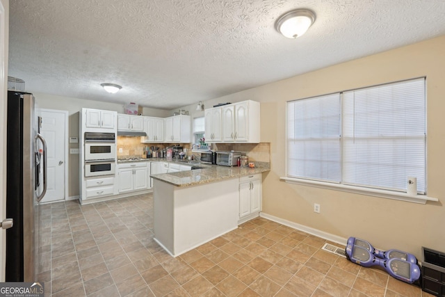 kitchen featuring visible vents, backsplash, white cabinetry, a peninsula, and stainless steel appliances