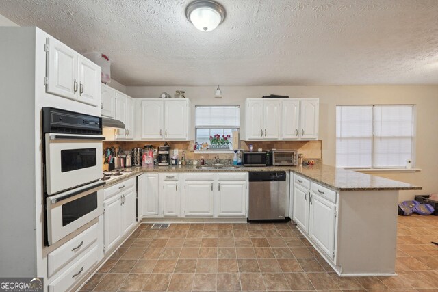 kitchen with a peninsula, white cabinets, appliances with stainless steel finishes, and a sink