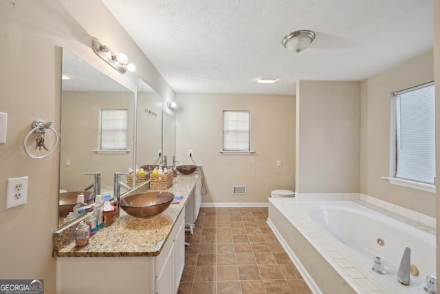 full bath featuring visible vents, baseboards, vanity, a whirlpool tub, and a textured ceiling