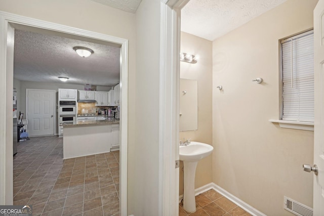 bathroom featuring visible vents, baseboards, tasteful backsplash, and a textured ceiling