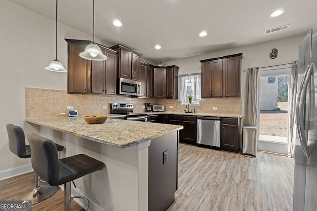 kitchen featuring visible vents, light wood-style floors, dark brown cabinetry, appliances with stainless steel finishes, and a peninsula