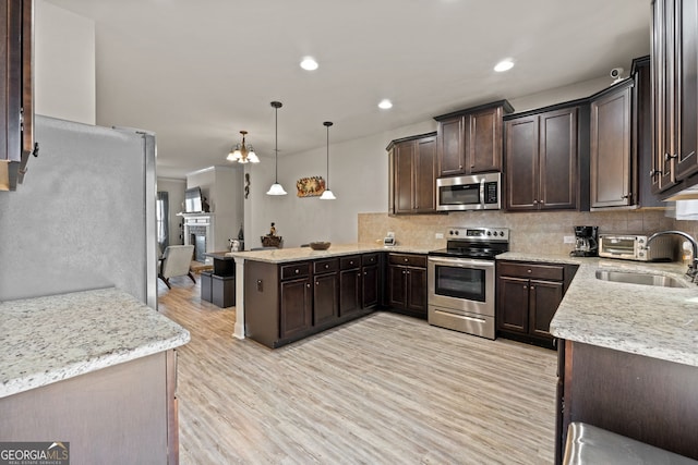 kitchen featuring a peninsula, a sink, decorative backsplash, stainless steel appliances, and dark brown cabinets