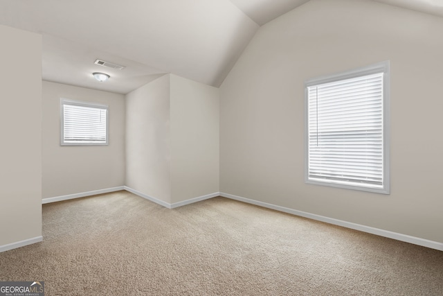 carpeted empty room with visible vents, baseboards, and vaulted ceiling