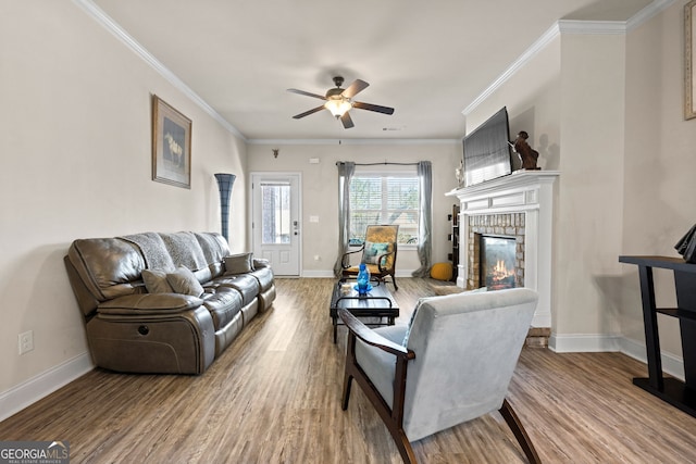 living area featuring baseboards, ornamental molding, a fireplace, wood finished floors, and a ceiling fan