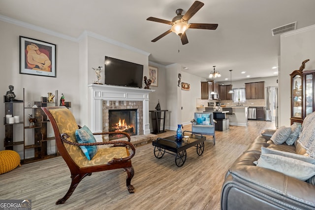 living area with light wood-type flooring, visible vents, a fireplace, crown molding, and ceiling fan