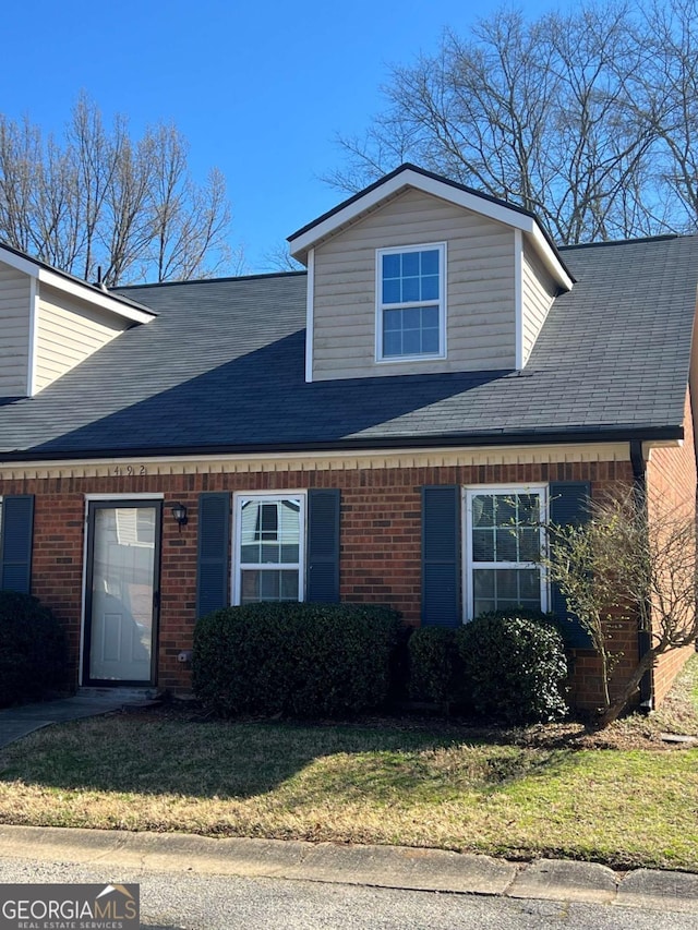 view of front of home with brick siding, roof with shingles, and a front yard