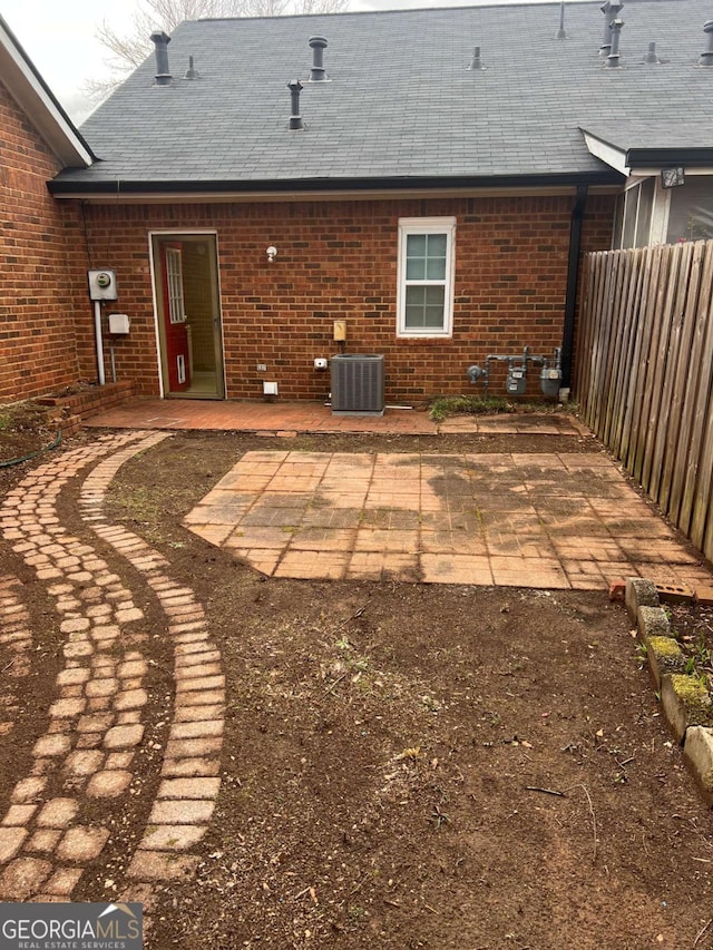 back of house with brick siding, fence, roof with shingles, cooling unit, and a patio area