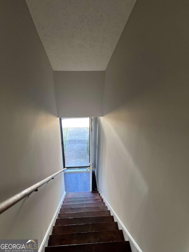 stairs with wood finished floors, baseboards, and a textured ceiling