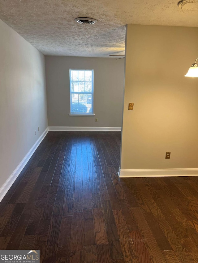 spare room featuring baseboards, dark wood-style flooring, and a textured ceiling