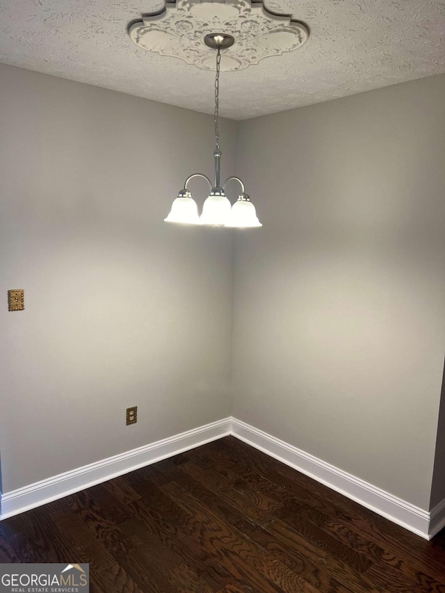 empty room featuring baseboards, dark wood-type flooring, and an inviting chandelier