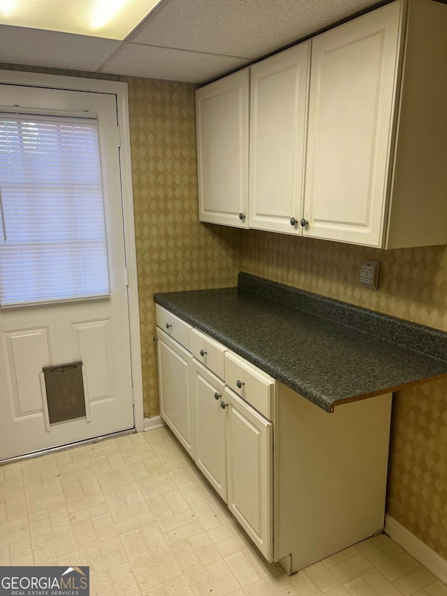 kitchen featuring dark countertops, wallpapered walls, baseboards, light floors, and white cabinetry