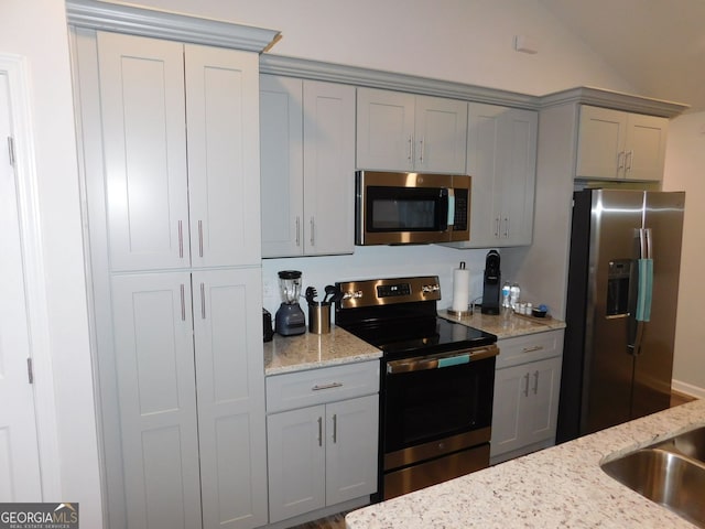 kitchen with vaulted ceiling, light stone counters, gray cabinets, and appliances with stainless steel finishes