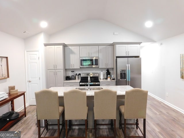 kitchen with a sink, stainless steel appliances, a breakfast bar, and vaulted ceiling