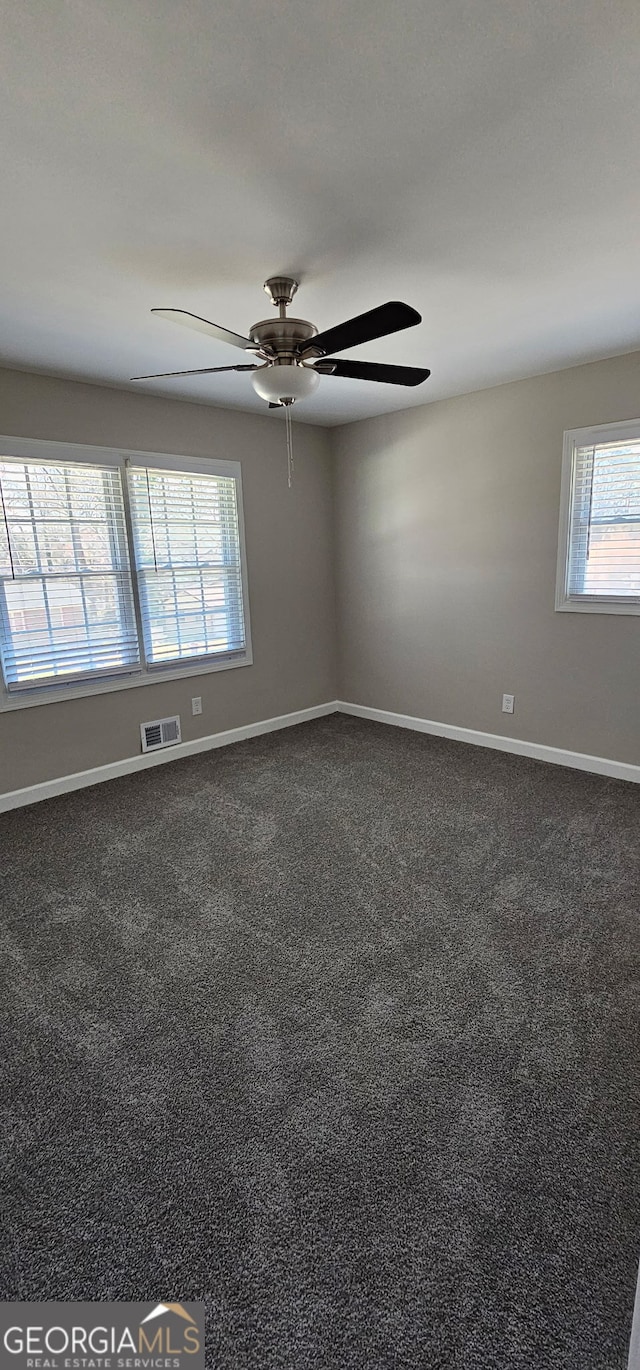 empty room with baseboards, visible vents, dark colored carpet, and ceiling fan