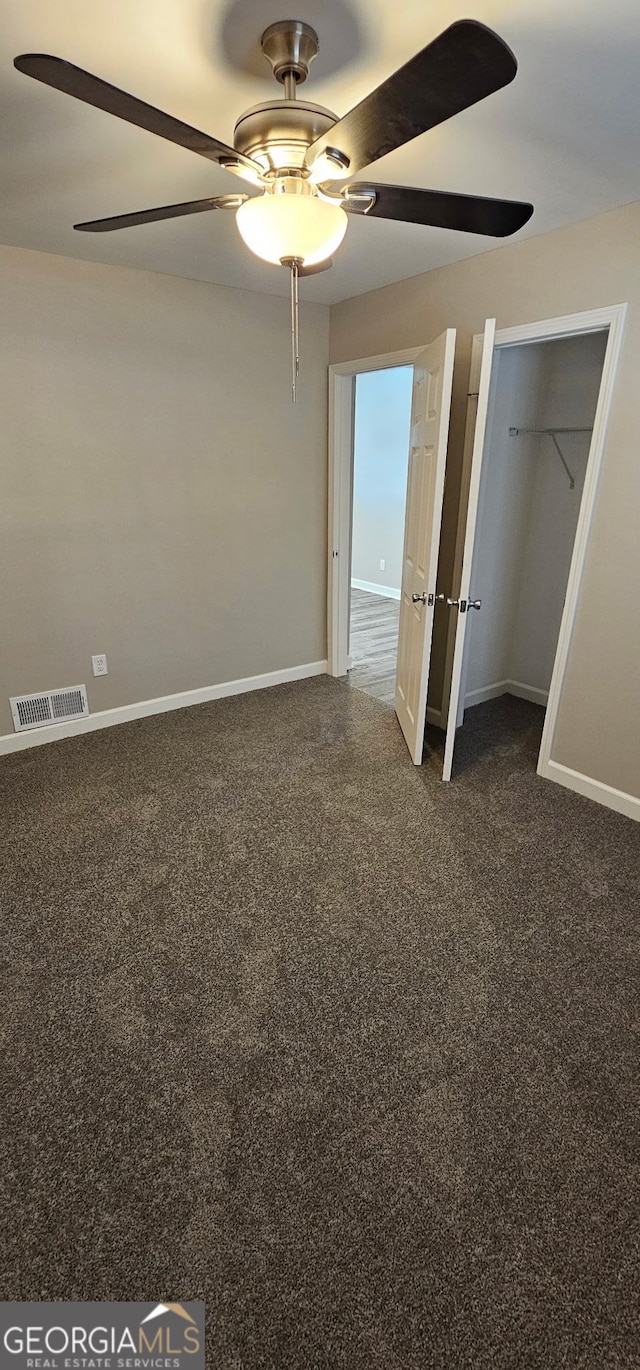 unfurnished bedroom with dark colored carpet, visible vents, baseboards, and ceiling fan