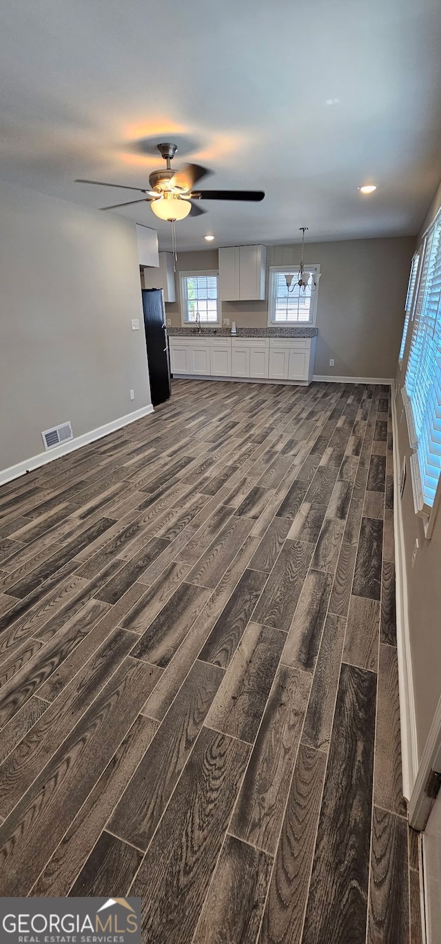 unfurnished living room featuring dark wood-style floors, visible vents, ceiling fan with notable chandelier, and baseboards