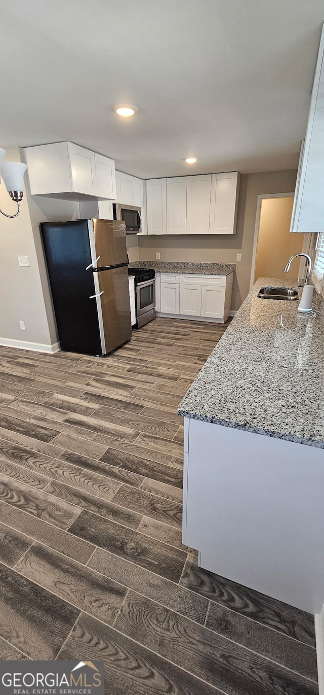 kitchen with stone counters, dark wood-style flooring, a sink, appliances with stainless steel finishes, and white cabinetry