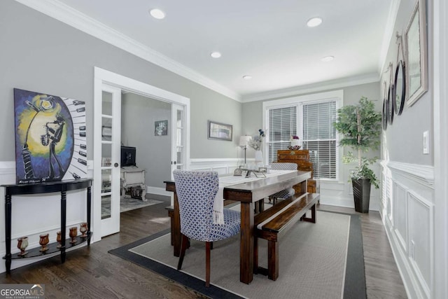 dining space featuring a decorative wall, wainscoting, wood finished floors, and ornamental molding